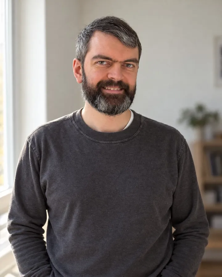 Pavlo Poliakov smiling, standing by a window in a grey sweater